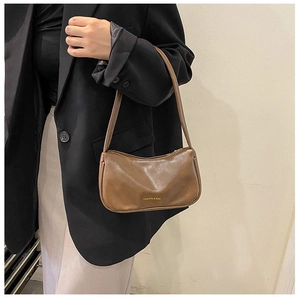 Brown leather baguette bag shown on shoulder over a black blazer for size perspective