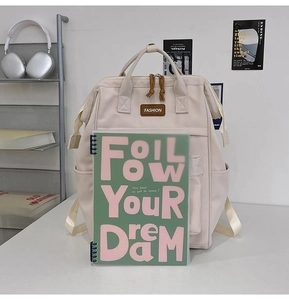 Large capacity beige Oxford backpack shown next to a notebook to illustrate its spacious size