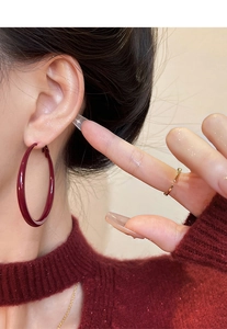 Detail of large burgundy hoop earring with smooth finish worn by a model in red knitwear