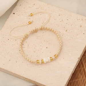 Detail of handmade woven seed bead bracelet with golden metal accents and cream pearls