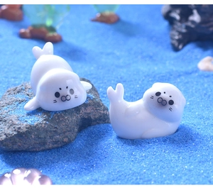 Miniature white cartoon sea lion figurines on blue sand for aquarium DIY decor