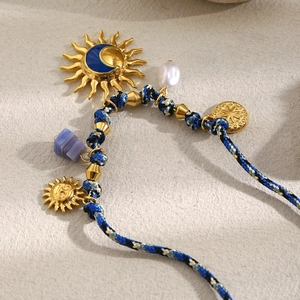 Detail of woven rope necklace with sun pendant, blue stone, and pearl in 18K gold finish