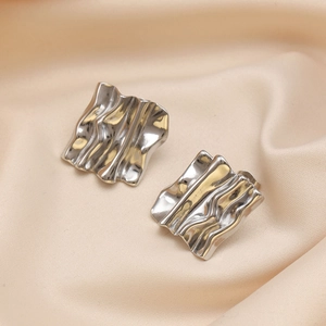 Macro shot of silver textured wavy stud earrings on soft beige silk background