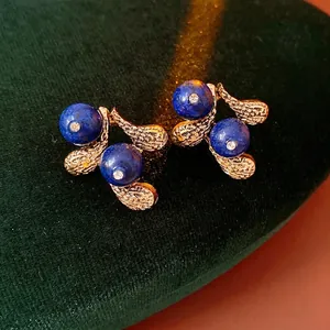 Vintage gold textured floral earrings set with deep blue gems on green velvet