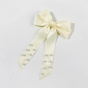 Detail view of a cream satin bow hair clip with elegant pearl embellishments on ribbons