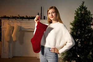 Close-up of a large red knitted Christmas stocking with tassel detail held by a model