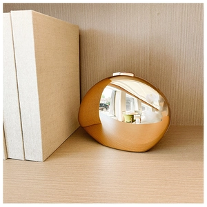 Detail of egg-shaped metal clutch with dual textured champagne gold matte and mirror finish