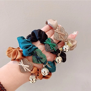 Close-up of four satin hair ties with crystal heart charms and silver beads on a hand