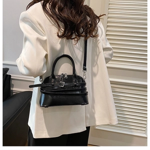 Detail of a black glossy shell bag with silver buckle strap worn with a white blazer