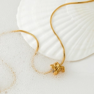 Golden irregular lava pendant necklace with sleek snake chain on white seashell background