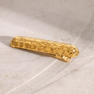 Nahaufnahme der goldenen Haarspange mit Hammerschlag-Optik auf einer Steinfläche