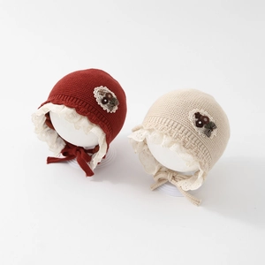 Infant knit bonnet with lace trim and bow detail in red and cream for autumn warmth