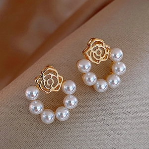 Close-up of golden rose earrings with white pearl semi-circles on a textured fabric