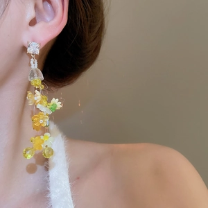 Close-up of dangling floral tassel earrings with yellow and green beads on model
