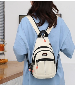 Detail view of cream sling bag featuring black zippers and bright orange pull tabs