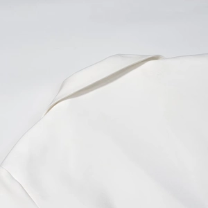 Close-up of the elegant deep V-neckline and shoulder details of this white blazer dress