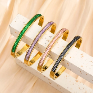 Detail of four gold stainless steel bracelets with emerald, purple, and black zircon gems