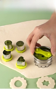Close-up of stainless steel cookie cutter set with green handles pressing on dough