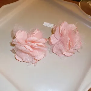 Detailed macro view of light pink organza flower earrings on a white ceramic tray