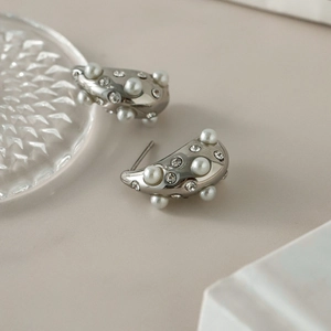 Silver teardrop stud earrings with inlaid white pearls and crystals on beige surface