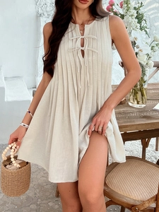 Detail of beige sleeveless pleated mini dress featuring front tie-up and linen texture