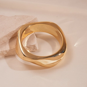 Close-up of a chunky irregular gold-plated bangle on a textured travertine stone base
