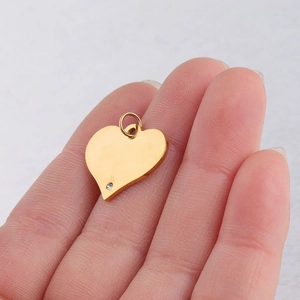 Close-up of golden heart pendant with a small diamond held between fingers for detail