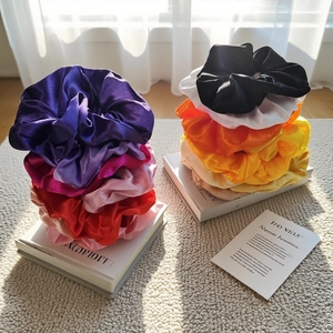 Multiple colorful satin silk scrunchies in various shades stacked on minimalist magazines