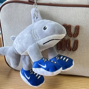 Close-up of a shark plush keychain in grey wearing blue sneakers on a beige canvas bag