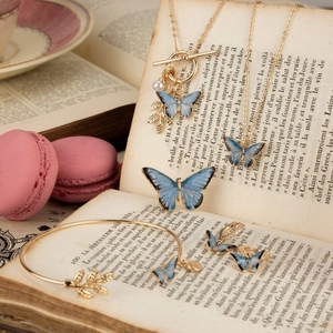 Parure bijoux romantique avec papillon bleu, feuilles dorées et perles sur vieux livre