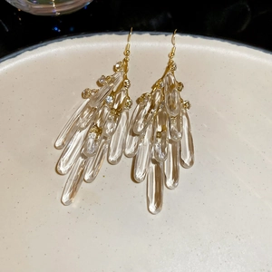 Detailed view of long gold tassel earrings with crystal teardrops on a ceramic plate