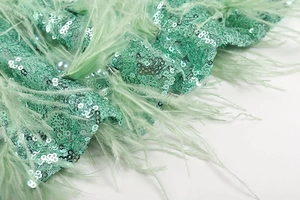 Detail of mint green sequin fabric with hand-sewn feathers and pearl embellishments