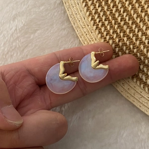 Macro view of C-shaped irregular gold earrings with lavender pearlescent texture details