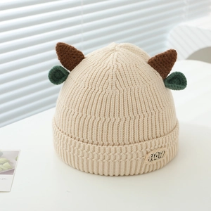 Detail of cream knit beanie featuring brown horns, green ears and Moo patch logo
