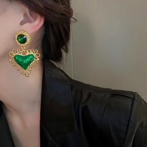 Close-up of vintage heart-shaped gold-framed green rhinestone earrings worn on the ear
