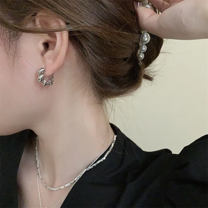 Detail van zilveren gedraaide oorringen en gelaagde ketting bij een model