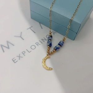 Detail of 18k gold plated moon pendant and blue marble bead on a light blue jewelry box