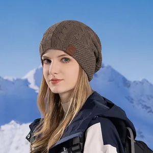 Winter thermal cable knit beanie for women featuring a faux leather patch on snowy background