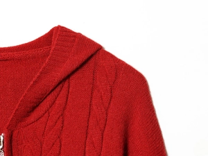 Détail d'un pull rouge en maille torsadée montrant la texture et la fermeture éclair en métal