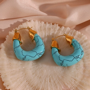 Macro detail of turquoise acrylic earrings with gold plating on a coral display