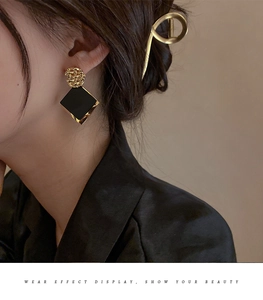 Detail view of geometric rhombus earrings with golden texture and black pendant on model