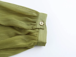 Close-up of green chiffon sleeve cuff with gold stripes and a metallic button detail