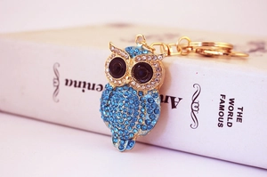 Close-up of owl keychain with blue rhinestones on an open book, gold metal finish