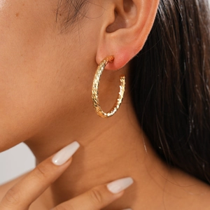 Close-up of golden geometric C-shaped hoop earring with textured diamond pattern on model