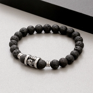 Macro detail of 8mm black lava stone beads and silver skull charm on a beaded bracelet