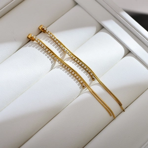 Macro detail of gold-plated tassel earrings with pavé zircons on white leather box