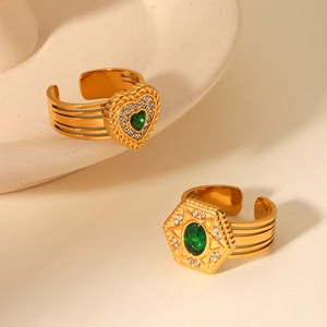 Detail of gold-plated heart and star rings with green stones on ceramic plate