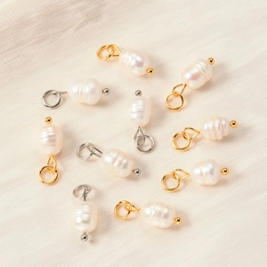 Baroque freshwater pearl pendants with gold and silver clasps on a textured background
