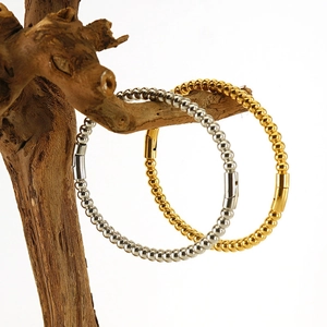 Detail of beaded stainless steel bracelets in gold and silver hung on a wood branch