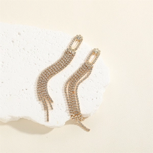 Golden fringe tassel earrings with sparkling rhinestones on a white decorative stone